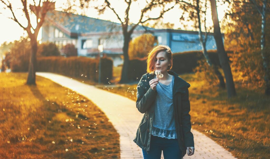 woman blowing dandelion flower standing on pathway